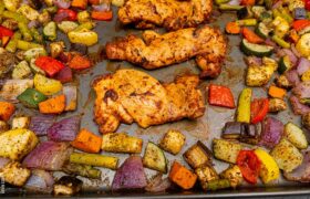 Kevin Curry’s sheet pan sriracha chicken thighs roasting with mixed vegetables like zucchini, peppers, and red onions.