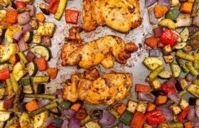 Kevin Curry’s sheet pan sriracha chicken thighs roasting with mixed vegetables like zucchini, peppers, and red onions.