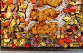 Kevin Curry’s sheet pan sriracha chicken thighs roasting with mixed vegetables like zucchini, peppers, and red onions.