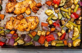 Kevin Curry’s sheet pan sriracha chicken thighs roasting with mixed vegetables like zucchini, peppers, and red onions.