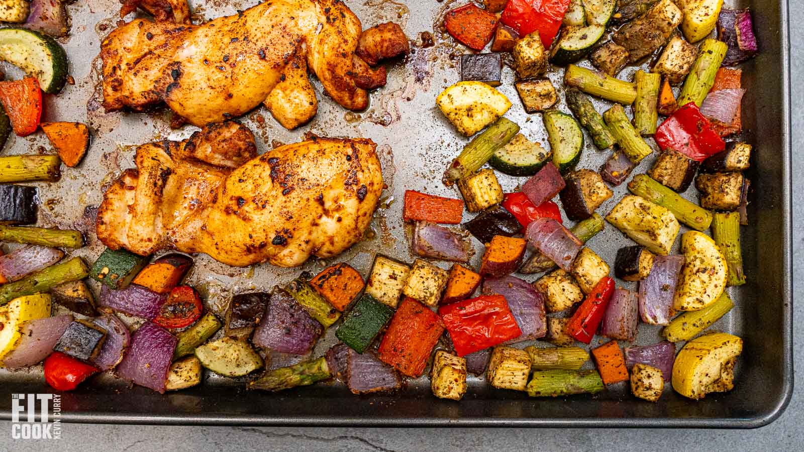 Kevin Curry’s sheet pan sriracha chicken thighs roasting with mixed vegetables like zucchini, peppers, and red onions.