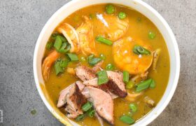 Close-up bowl of creamy Caribbean seafood soup with shrimp, flaked salmon, green peas, and scallions