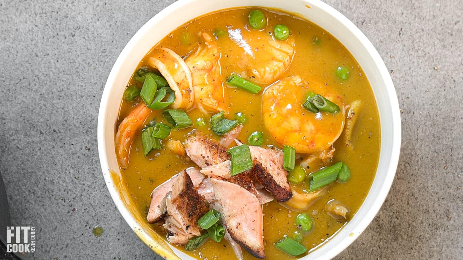 Close-up bowl of creamy Caribbean seafood soup with shrimp, flaked salmon, green peas, and scallions