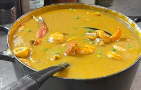 Close-up of sweet potato coconut seafood soup with seared scallop, shrimp, crab claw, and peas in a black Dutch oven