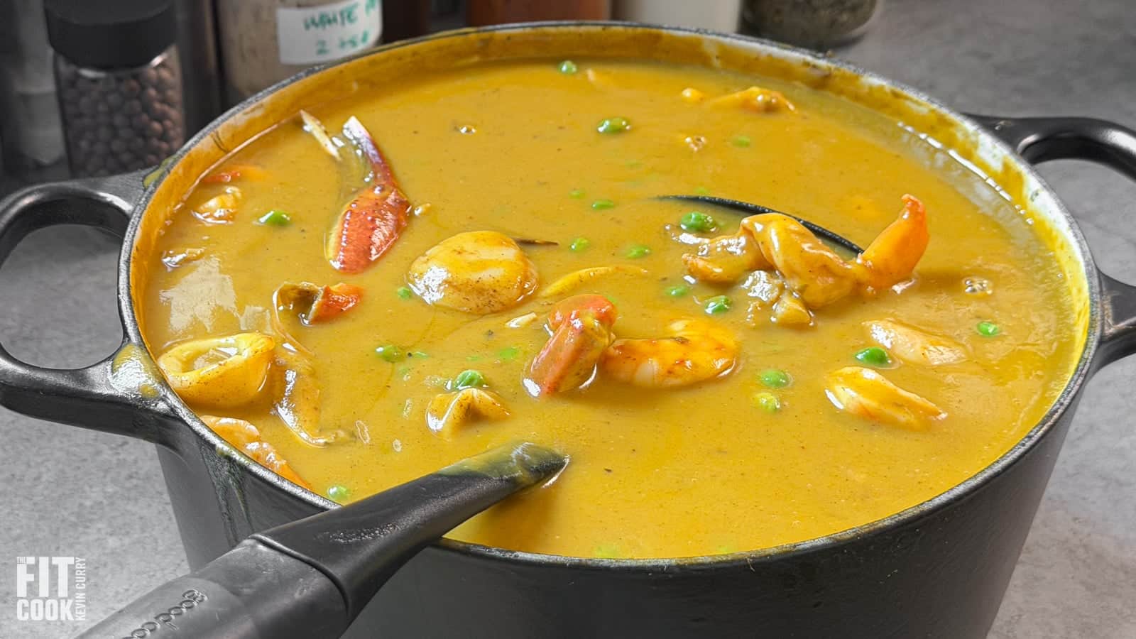 Close-up of sweet potato coconut seafood soup with seared scallop, shrimp, crab claw, and peas in a black Dutch oven