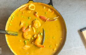 Overhead view of creamy Caribbean seafood soup in a Dutch oven with shrimp, scallops, crab claw, green peas, and a whole scotch bonnet