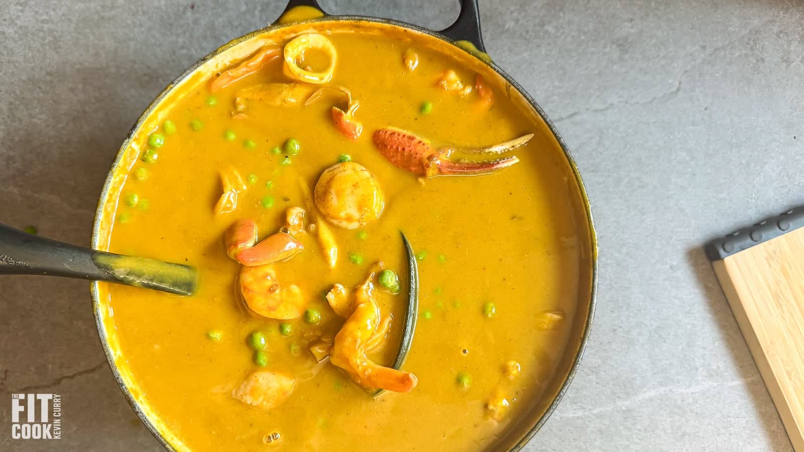 Overhead view of creamy Caribbean seafood soup in a Dutch oven with shrimp, scallops, crab claw, green peas, and a whole scotch bonnet