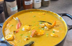 Pot of dairy-free Caribbean seafood soup with shrimp, scallops, and crab in front of labeled spice jars