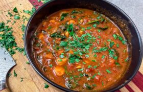Harissa chickpea stew with dino kale in a bowl, cinnamon stick on the side